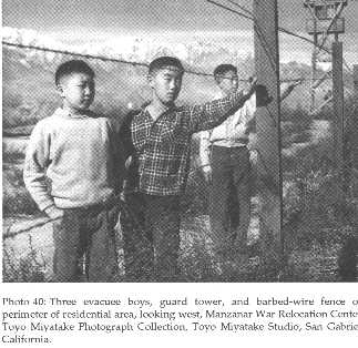 Three evacuee boys, guard tower, and barbed-wire fence on the perimeter of the residential area at Manzanar War Relocation Center